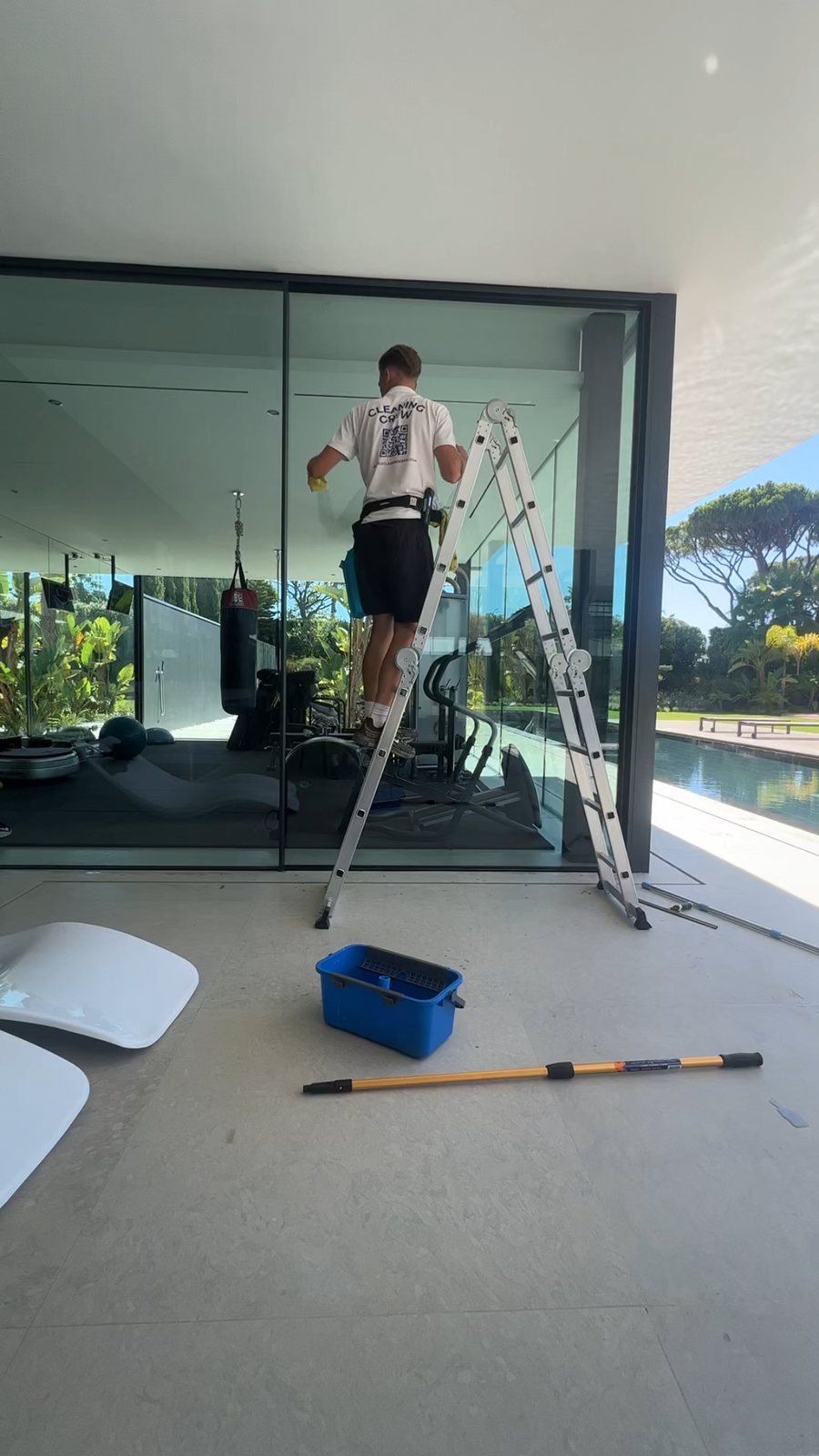 Cleaning floor-to-ceiling sliding doors from a ladder at a Vale do Lobo villa