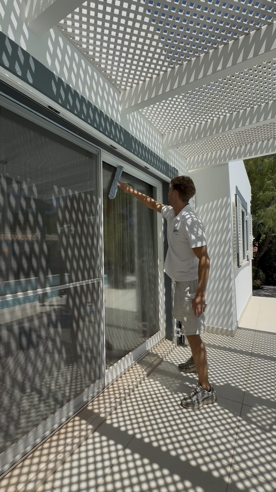 Cleaning villa glass under a perforated pergola in Quinta do Lago