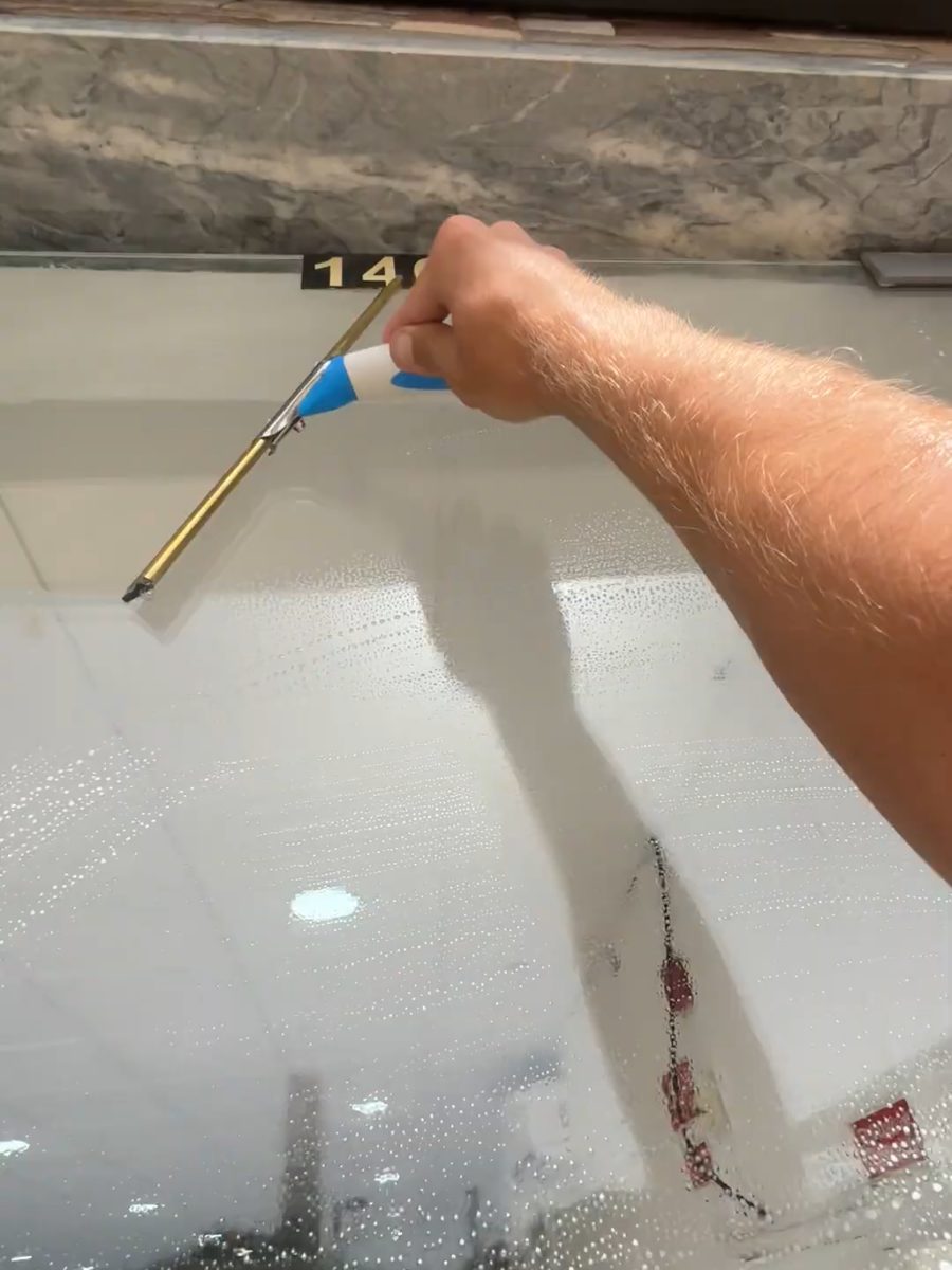 Squeegee starting a pull at the top of a soaped shopfront pane in Almancil